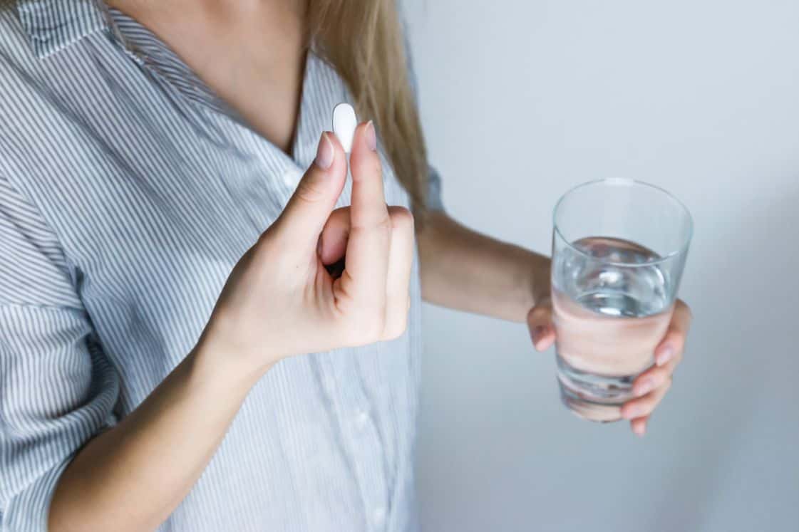 Kobieta trzymająca w ręku tabletkę i szklankę wody