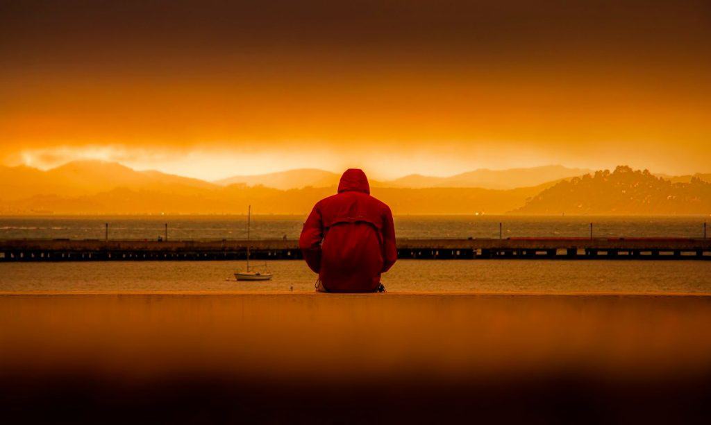 Mężczyzna w kapturze siedzący na brzegu morza